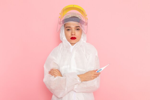 young beautiful female in special white suit wearing protective helmet holding device on pink