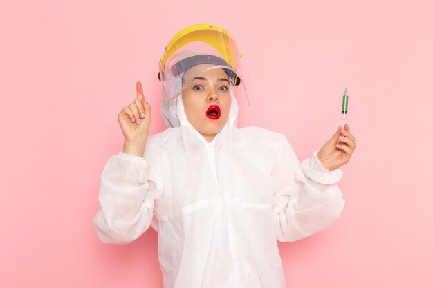 young beautiful female in special white suit wearing protective helmet holding injection on pink