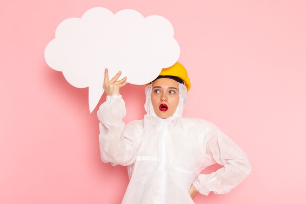 young beautiful female in special white suit and yellow helmet holding big white sign on pink