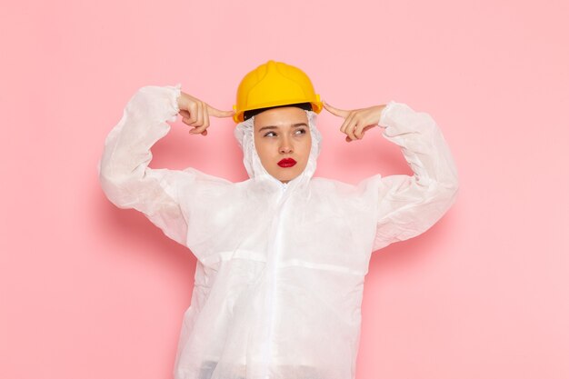 young beautiful female in special white suit and yellow helmet thinking on pink