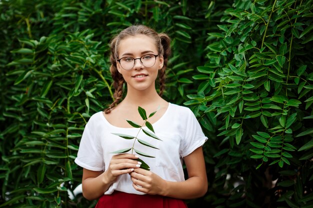 Молодая красивая студентка в очках, улыбаясь, позирует на листьях на открытом воздухе.