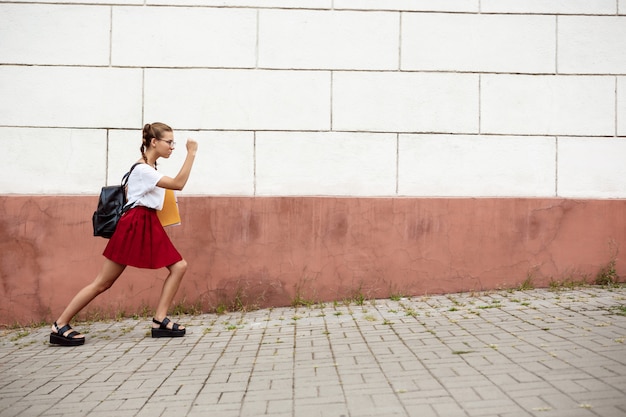 Foto gratuita giovane bella studentessa in bicchieri camminando per strada, tenendo le cartelle