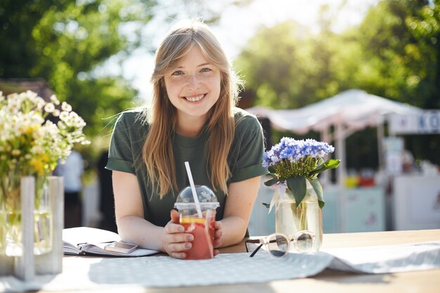 Young beautiful female student taking a break from classes drinking grapefruit lemonade smiling