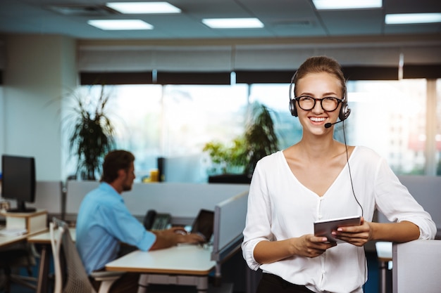 Foto gratuita giovane bello operatore telefonico femminile di sostegno che parla, consultando, sopra l'ufficio