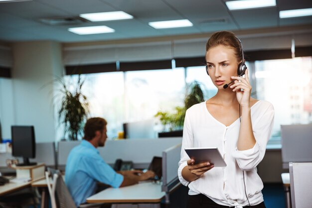 Young beautiful female support phone operator speaking, consulting, over office