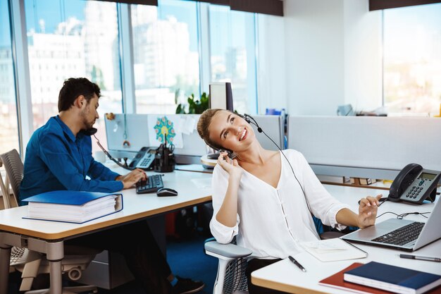 Young beautiful female support phone operator speaking, consulting, over office