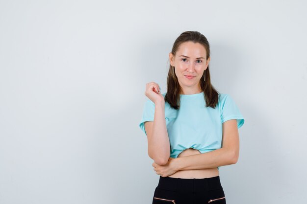 立って陽気に見ながらポーズをとるTシャツの若い美しい女性、正面図。