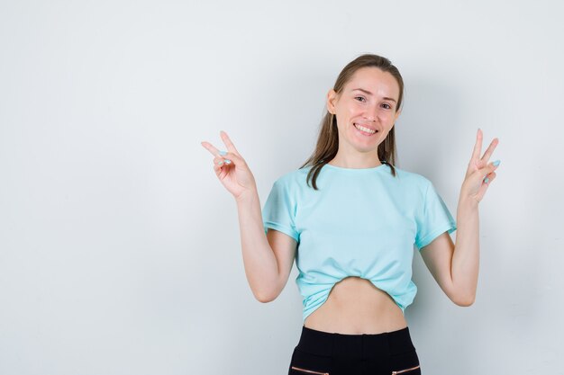 Young beautiful female in t-shirt showing victory sign and looking blissful , front view.
