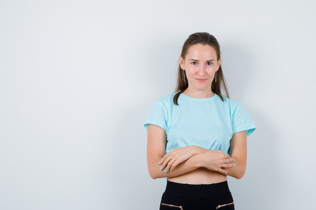 Young beautiful female with arms folded in t-shirt and looking merry , front view.