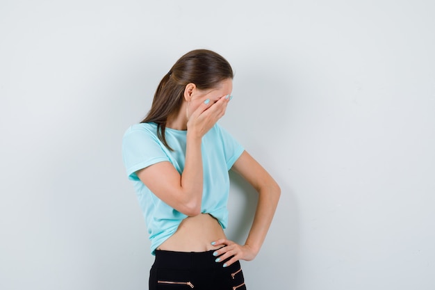 Young beautiful female with hand on face in t-shirt and looking cheerless. front view.