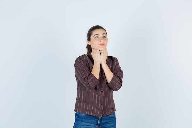 Young beautiful female with hands under chin in jacket and looking hopeful , front view.