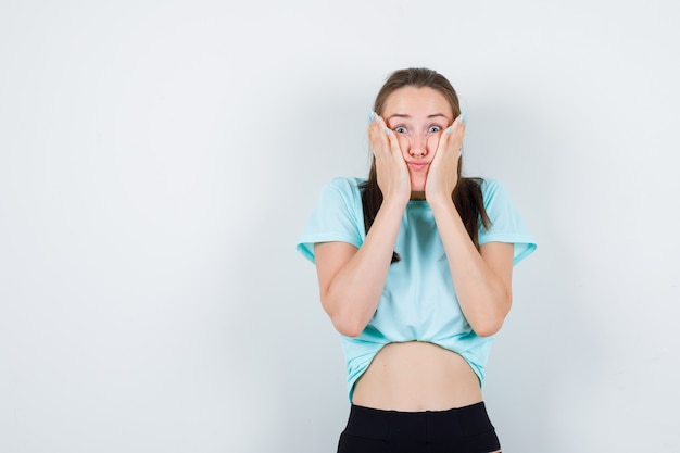 Young beautiful female with hands on face in t-shirt and looking bored. front view.