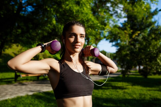 young beautiful fitness girl holding dumbbells at nature