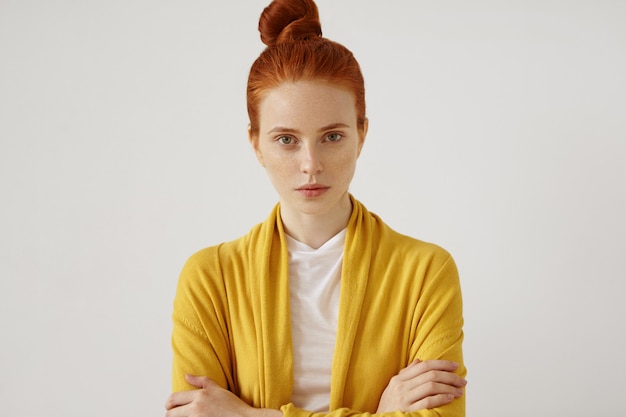 Young beautiful freckled woman with red hair tied in bun, wearing bright clothes, keeping hands crossed, looking confidently, isolated. beauty and youth concept