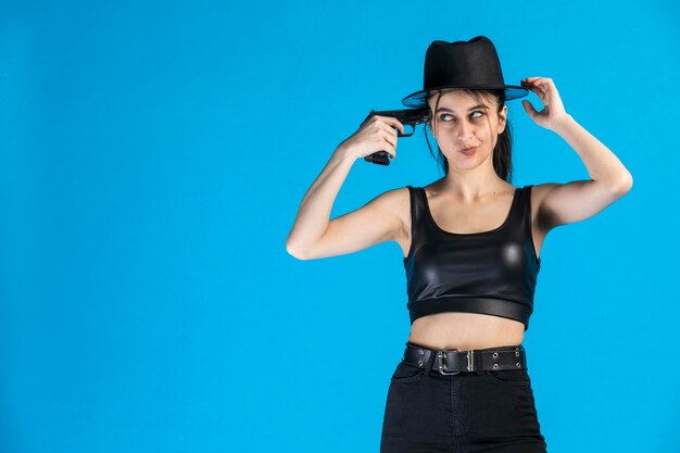 Young beautiful gangster put her gun to her head and standing on blue background