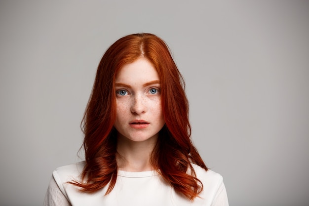 young beautiful ginger girl over gray wall.