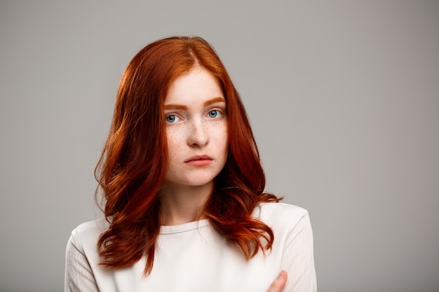 young beautiful ginger girl over gray wall.