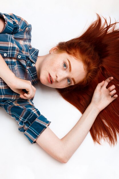 young beautiful ginger girl lauing down over white wall.