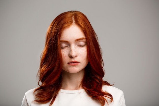 young beautiful ginger girl with eyes closed over gray wall.