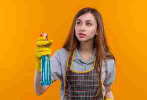 Free photo young beautiful girl in apron holding cleaning spray looking aside ,going to clean