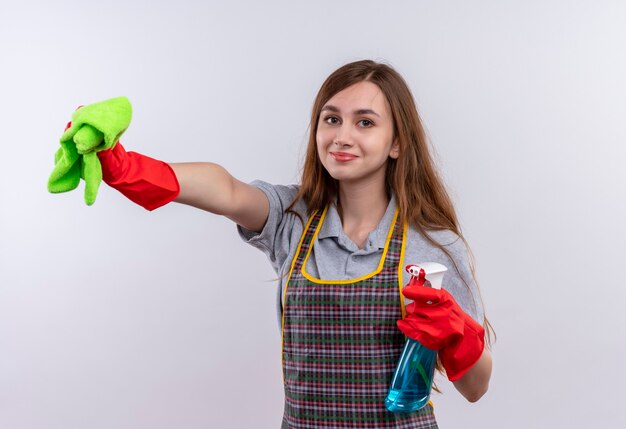 Giovane bella ragazza in grembiule azienda spray per la pulizia e tappeto guardando sorridente della fotocamera, pronta per la pulizia