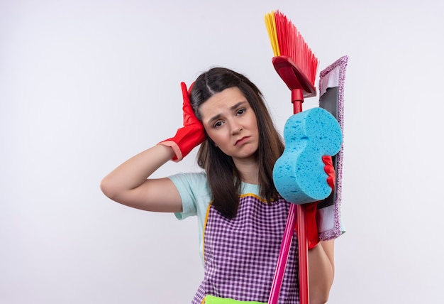 Free photo young beautiful girl in apron and rubber gloves holding cleaning tools looking tired and overworked having headache