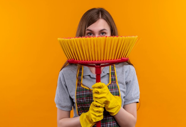 Free photo young beautiful girl in apron and rubber gloves holding mop hading face behind it peeking over