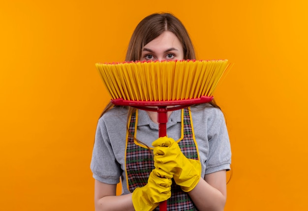 Foto gratuita giovane bella ragazza in grembiule e guanti di gomma che tengono la faccia di hading del mop dietro esso che dà una occhiata sopra