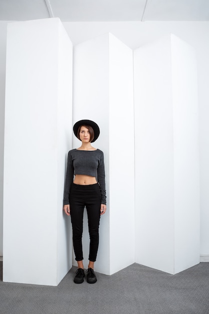 Free photo young beautiful girl in black hat posing over white wall