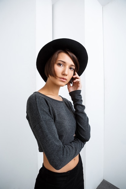 Young beautiful girl in black hat posing over white wall