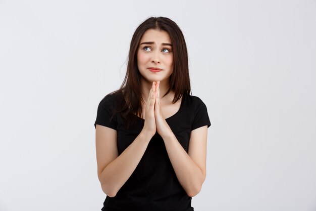 Молодая красивая девушка в черной футболке с надеждой молится над белой стеной