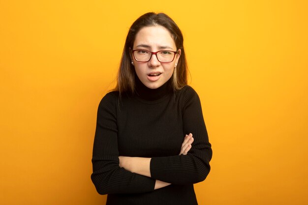 Young beautiful girl in a black turtleneck being confused and displeased with arms crossed on chest 