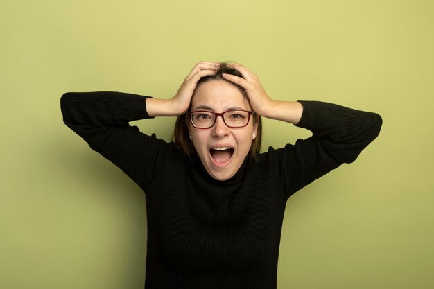 Free photo young beautiful girl in a black turtleneck and glasses shouting and yelling going wild pulling her hair