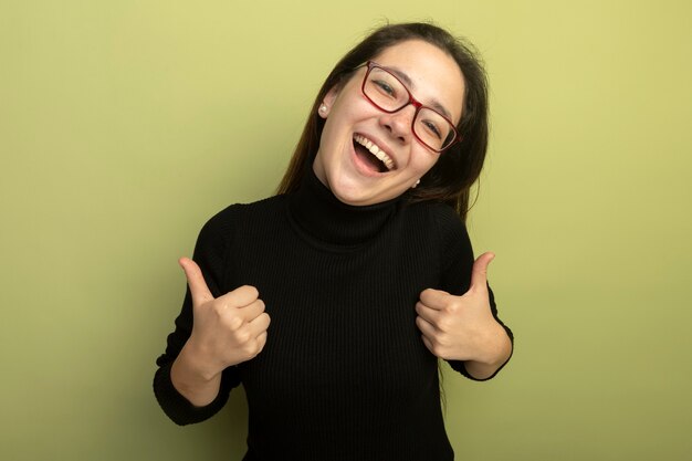 Young beautiful girl in a black turtleneck and glasses smiling with happy face showing thumbs up 