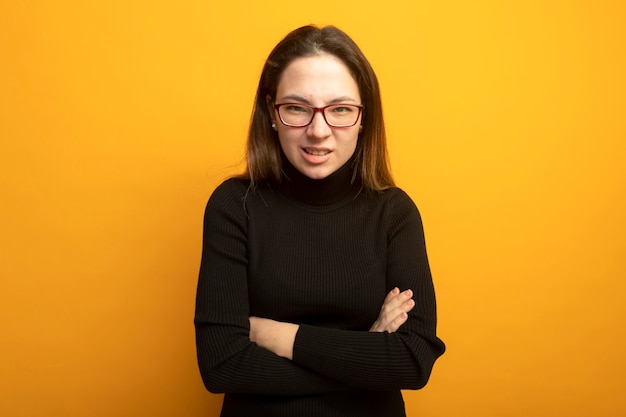 Young beautiful girl in a black turtleneck lookign at camera being displeased with arms crossed on chest 