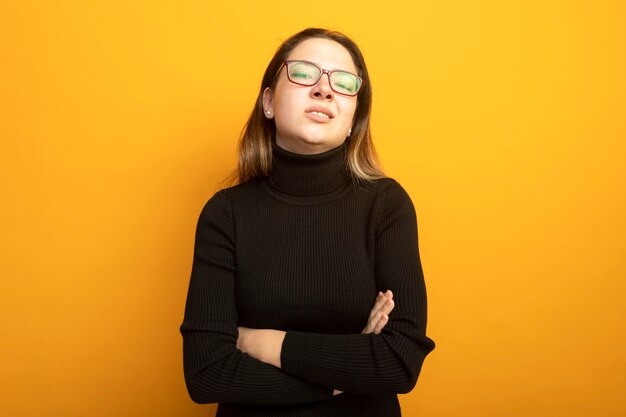 Young beautiful girl in a black turtleneck self-satisfied with confident expression with arms crossed on chest 