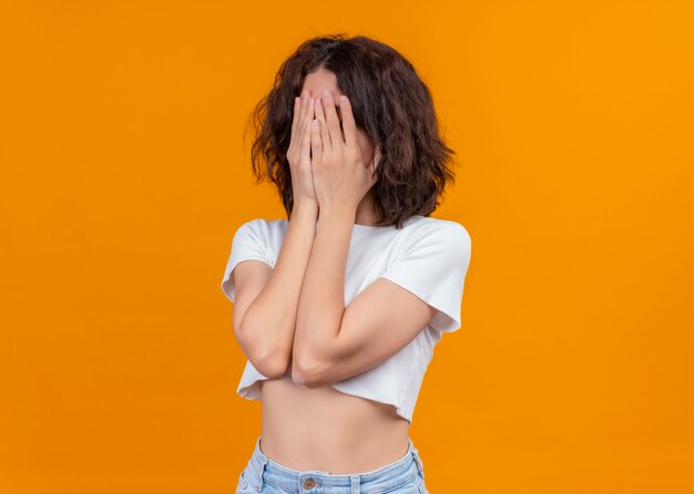 Young beautiful girl closing her face with hands on isolated orange background with copy space