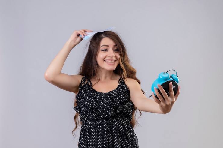 मुफ़्त फोटो young beautiful girl in dress in polka dot holding alarm clock and tickets smiling cheerfully positive and happy standing over white background