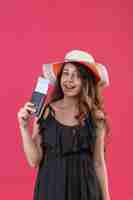 Free photo young beautiful girl in dress in polka dot in summer hat holding air tickets looking at camera smiling cheerfully standing over pink background