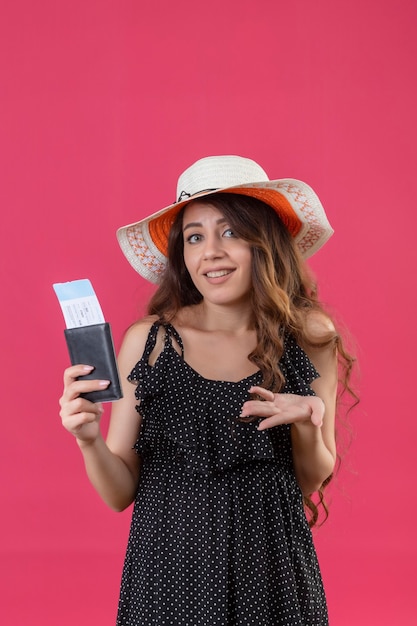 분홍색 배경 위에 서 혼란 스 러 워 항공 티켓을 들고 여름 모자에 폴카 도트 드레스에서 젊은 아름 다운 소녀
