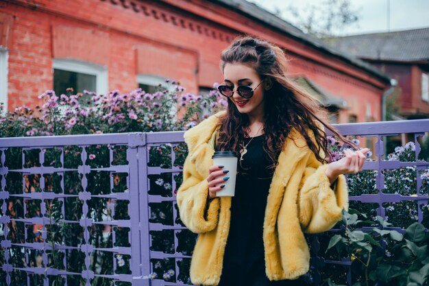 young beautiful girl drinks coffee in a glass on the street, laughs and smiles