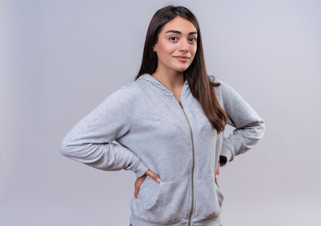 Young beautiful girl in gray hoody looking at camera confident smile on face standing over white background