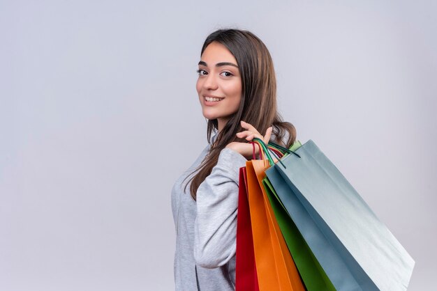 Young beautiful girl in gray hoody looking at camera with smile on face holding packages standing over white background