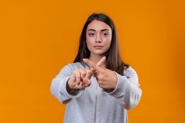 Young beautiful girl in gray hoody making x gesture standing over orange background