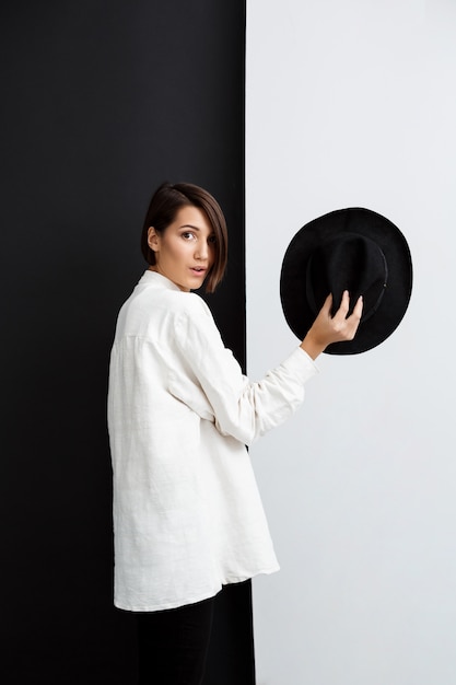 Free photo young beautiful girl holding hat over black and white wall