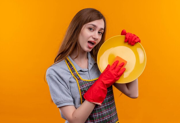 Бесплатное фото Молодая красивая девушка в фартуке и резиновых перчатках моет тарелку с помощью губки