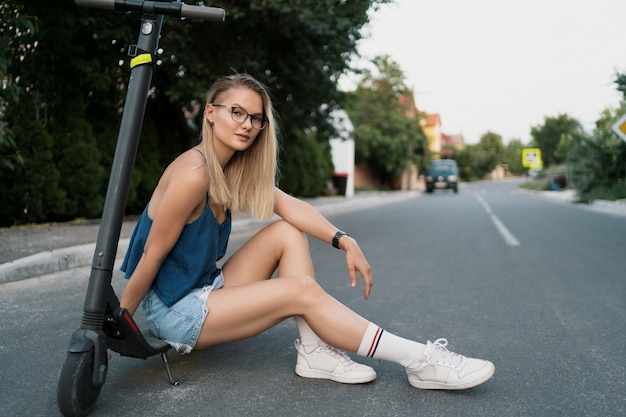 Free photo young beautiful girl is sitting on her electro scooter in the summer on the street