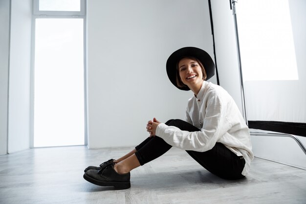 Young beautiful girl laughing sitting on floor over white wall.