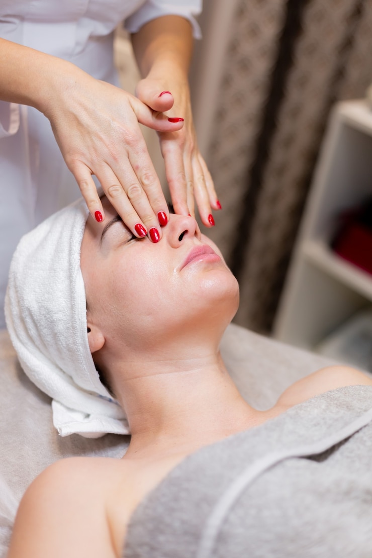 Free Photo a young beautiful girl lies on the beautician's table and receives procedures, a light facial massage using oil.