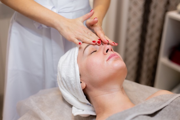 A young beautiful girl lies on the beautician's table and receives procedures, a light facial massage using oil.